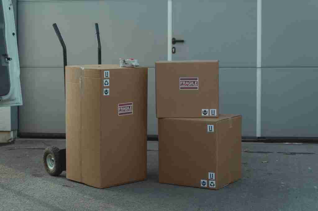 Tres cajas de cartón con etiquetas «Frágil» junto a un carrito de transporte de mano ante una puerta de garaje